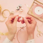 Jewelry designer workplace. Woman hands making handmade jewelry. Freelance fashion femininity workspace in flat lay style. Pastel pink and gold
